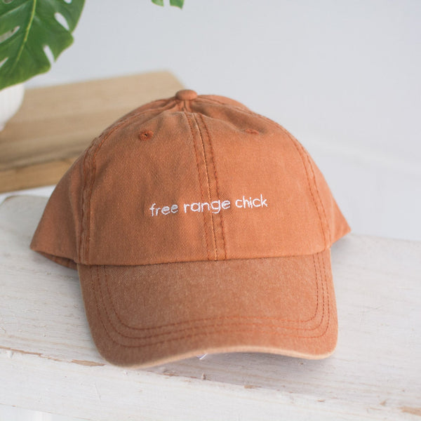 Brown cap with 'free range chick' text on a white surface with a plant in the background
