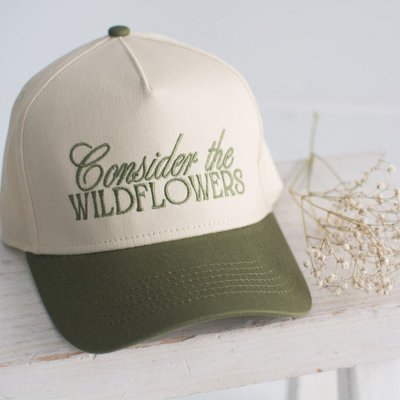 Beige and green cap with 'Consider the Wildflowers' text on a white surface.