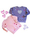 Two children's sweatshirts, one pink and one blue, with heart designs on a white background.